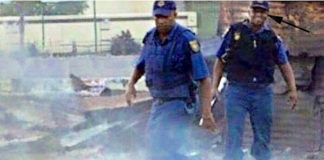 A picture taken in South Africa recently during the on-going clashes shows two South African policemen, with one of the law enforcers, see arrow, seemingly laughing at the burning victim. NET PHOTO